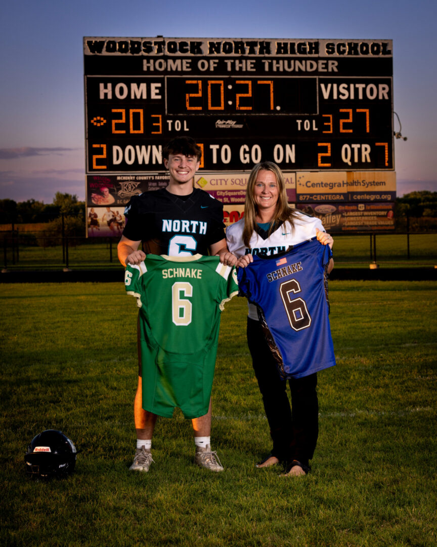 Two athletes holding matching jerseys on field.