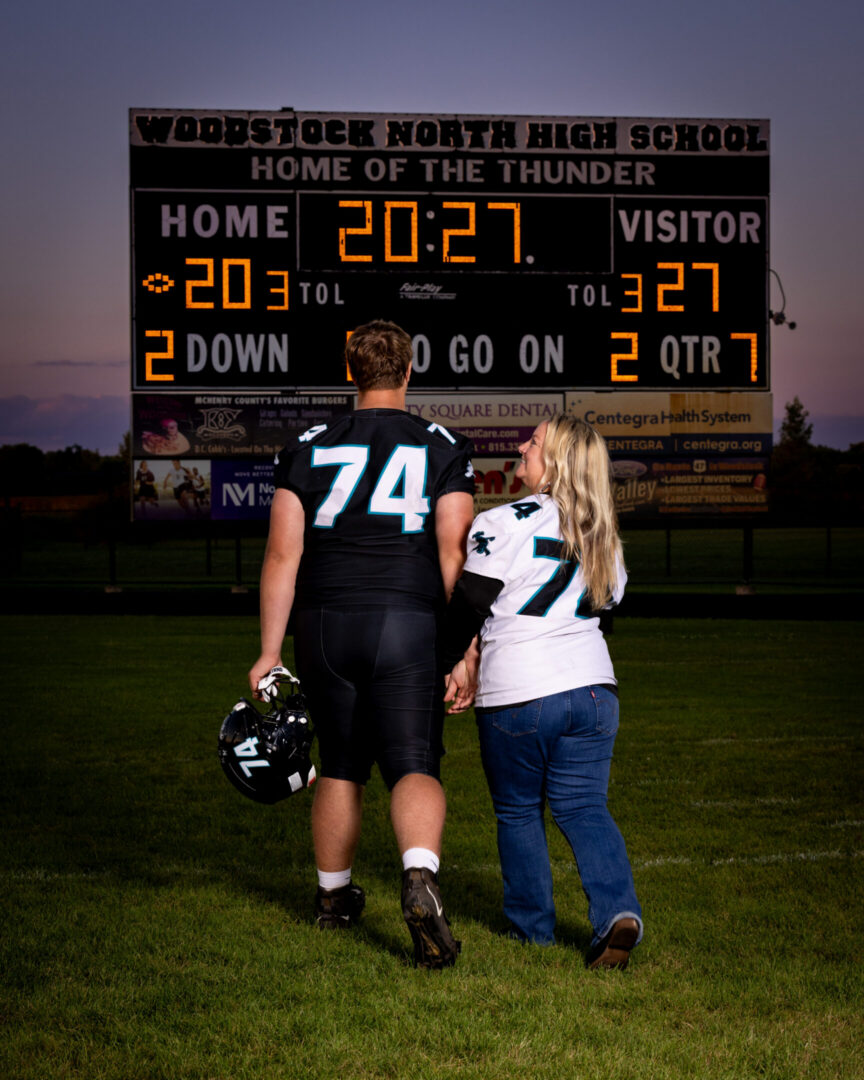 Couple walking hand-in-hand on football field.